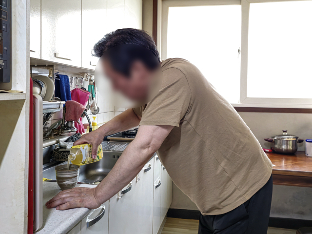 박상호(65·가명) 씨가 척추협착증과 척추전방전위증 때문에 고통스러워하며 몇 걸음도 떼기 힘든 몸으로 부엌에서 끼니를 챙기려 하고 있다. 김지효 기자