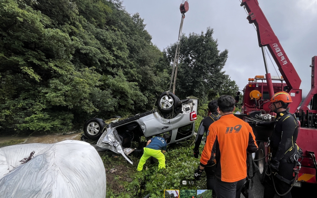 19일 경남 밀양시 조천면 급류에 휘말린 SUV 차량을 소방대원들이 중장비를 동원해 건져내고 있다. 경남소방본부 제공