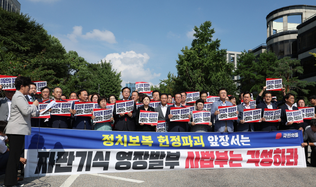 국민의힘 송언석 비상대책위원장 겸 원내대표를 포함한 의원들이 18일 서울 서초구 서울중앙지방법원 앞에서 열린 현장비상의원총회에서 손팻말을 들고 있다. 연합뉴스
