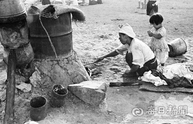 1955년 여름날 대구 팔달교 아래 금호강 백사장에서 한 아낙네가 드럼통을 잘라 만든 솥에 빨래를 삶고 있다. 사진=매일아카이빙센터
