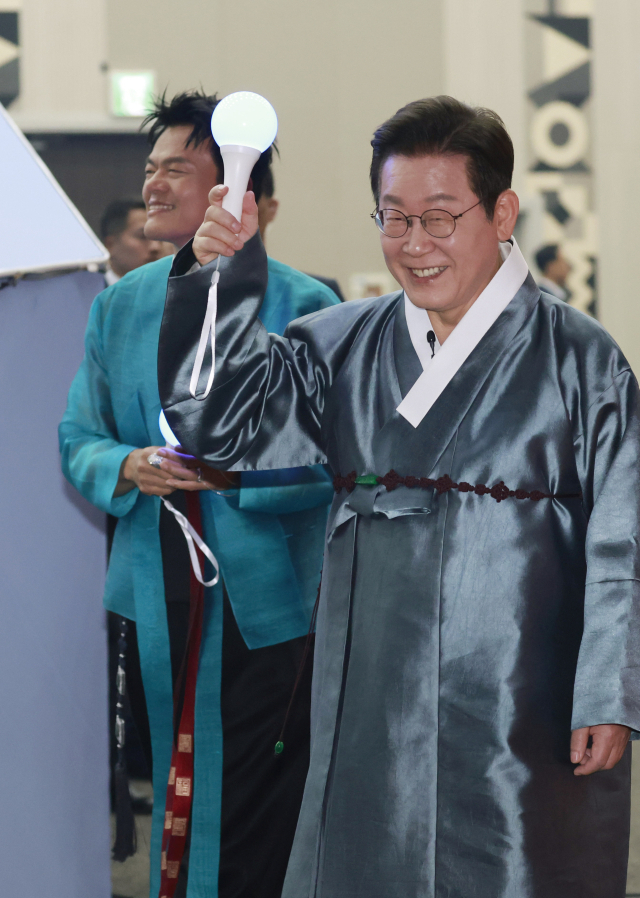 이재명 대통령이 1일 경기 고양시 킨텍스에서 열린 대중문화교류위원회 출범식에서 응원봉을 들고 문화공연 행사장에 입장하고 있다. 왼쪽은 박진영 공동위원장. 연합뉴스