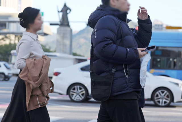 쌀쌀한 아침 날씨가 이어지는 지난 22일 서울 광화문광장에서 패딩을 입은 시민과 겉옷을 벗은 시민이 나란히 걸어가고 있다. 연합뉴스