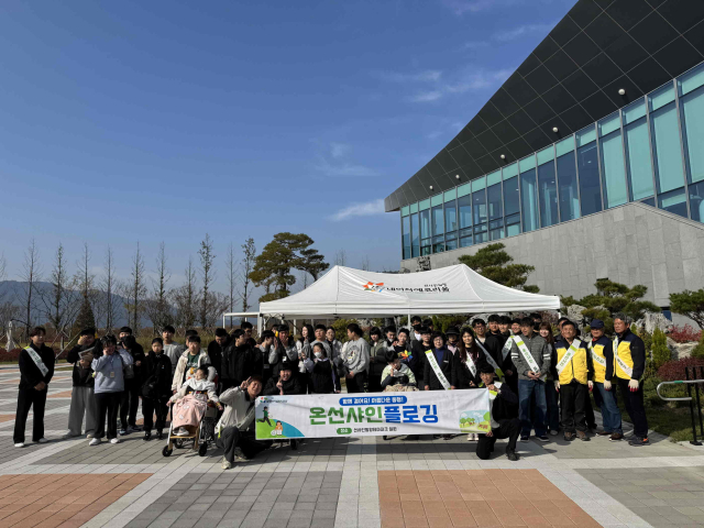 밀양시시설관리공단과 김해 은혜학교 학생들이 선샤인 밀양 테마파크 일대에서 환경정화 활동 후 단체 기념 촬영을 하고 있다.