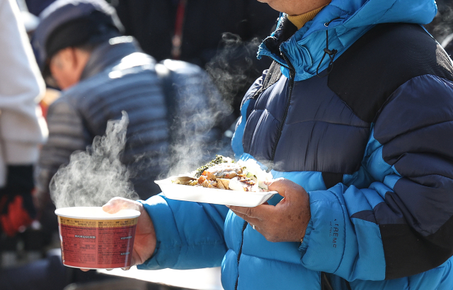올가을 가장 추운 날씨를 보인 지난 18일 대구 달서구 두류공원 사랑해밥차 무료 급식소에서 어르신들이 따뜻한 밥을 받아 이동하고 있다. 연합뉴스