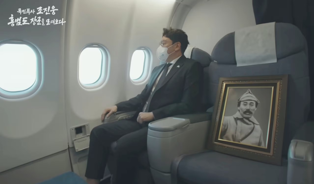 문재인 정부 시절이던 2021년 8월 국민 특사 자격으로 카자흐스탄에서 홍범도 장군 유해를 가져오고 있는 배우 조진웅. 옆자리에 홍범도 장군 영정이 놓여있다. KBS