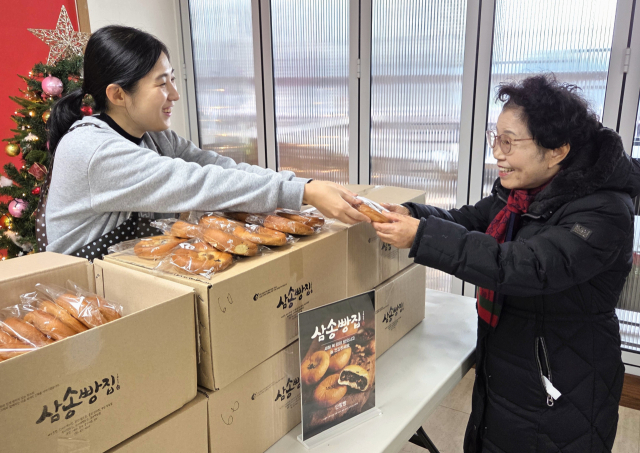 상송빵집 직원이 대구실버대학 행복밥상에서 어르신에게 빵을 전달해주고 있다. 삼송빵집 제공