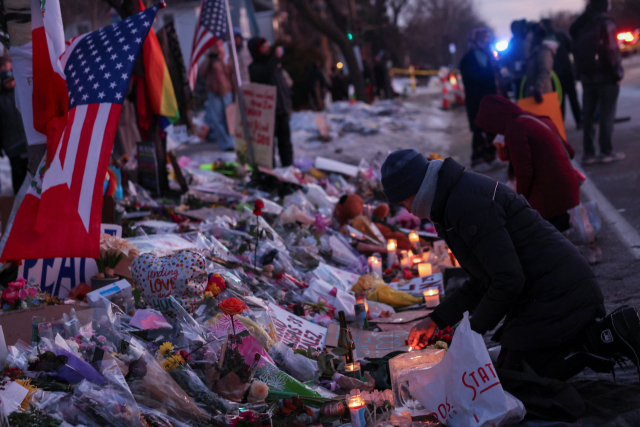 11일(현지시간) 미국 미네소타주 미니애폴리스에서 이민세관단속국(ICE) 요원이 쏜 총에 숨진 르네 니콜 굿의 사고 현장에 임시 추모비가 마련돼 있다. 그 앞을 추도하는 시민들이 꽃을 놓으며 무릎을 꿇고 있다. 로이터 연합뉴스