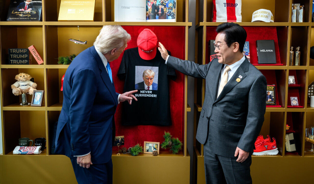 지난 2025년 10월 한미정상회담을 위해 경북 경주를 찾았던 도널드 트럼프 미국 대통령이 이재명 대통령과 정상회담에 앞서 경주박물관에 전시된 자신의 굿즈 전시품을 관람하고 있다. 두 정상이 함께 바라보고 있는 티셔츠 속 사진은 트럼프 대통령이 조 바이든 행정부 때 대선 뒤집기 시도 혐의 등으로 기소돼 2023년 미 조지아 주 풀턴 카운티 검찰에 출두했을 당시 찍은 머그샷(범인 식별용 사진)이다. 이 머그샷 티셔츠는 팬덤의 호응을 얻으며 불티나게 팔렸고 트럼프의 재선 성공 발판으로도 평가된다. 이날 만남은 미국에서 가장 큰 정치팬덤을 보유한 트럼프 대통령이 자신의 정치 위기 극복 상징을 한국에서 역시 가장 큰 정치팬덤을 가진 이재명 대통령에게 자랑한 맥락이기도 하다. 미 백악관 X(구 트위터)