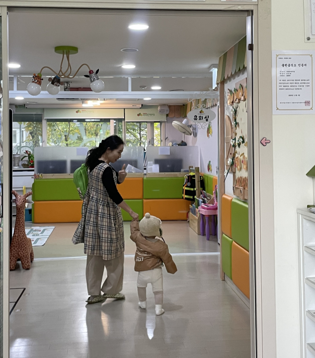 어린이집 선생님(왼쪽) 손을 잡고 뒤도 돌아보지 않고 어린이집으로 향하는 한태서(오른쪽) 어린이. 사진 밖에는 태서를 배웅하는 엄마가 웃고 있다.
