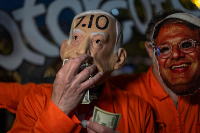 4일(현지시간) 이스라엘 텔아비브에서 열린 이란전쟁 반대 시위에서 베냐민 네타냐후 총리(왼쪽)의 얼굴이 그려진 가면을 쓴 시위 참가자가 달러를 먹는 시늉을 하고 있는 모습. AFP 연합뉴스