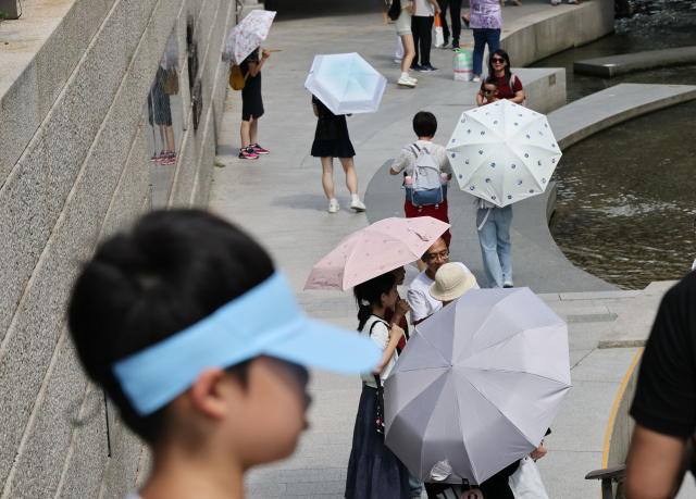 서울 전역에 폭염주의보가 발효된 26일 서울 청계천에서 시민들이 양산을 쓰고 이동하고 있다. 연합뉴스