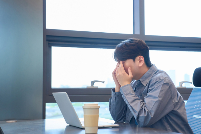 한 남성이 노트북 앞에서 피곤한 표정으로 얼굴을 감싸고 있다. 게티이미지뱅크